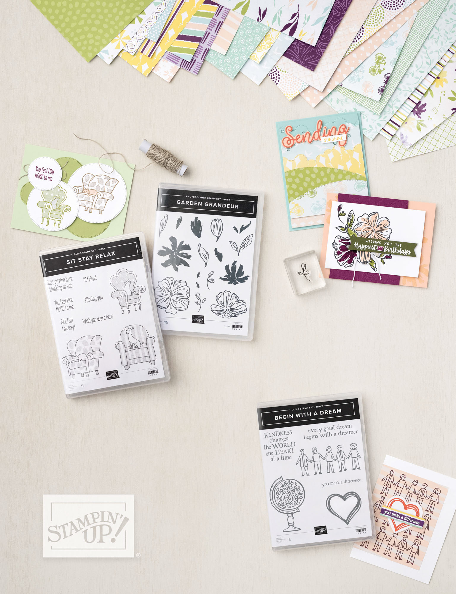 Stampin’ Up! cardmaking setup with three German-language stamp sets, coordinating handmade cards, and a spread of colorful patterned papers. Projects include stamped images like armchairs, flowers, and people holding hands, showcasing playful and heartfelt designs.